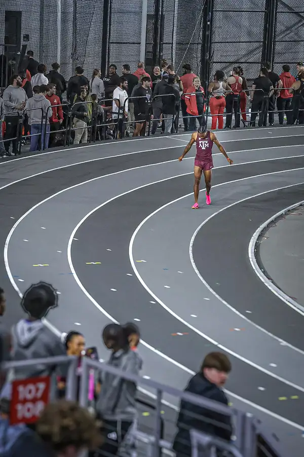 Lone runner on the curve of an indoor track, crowd packed along the rail