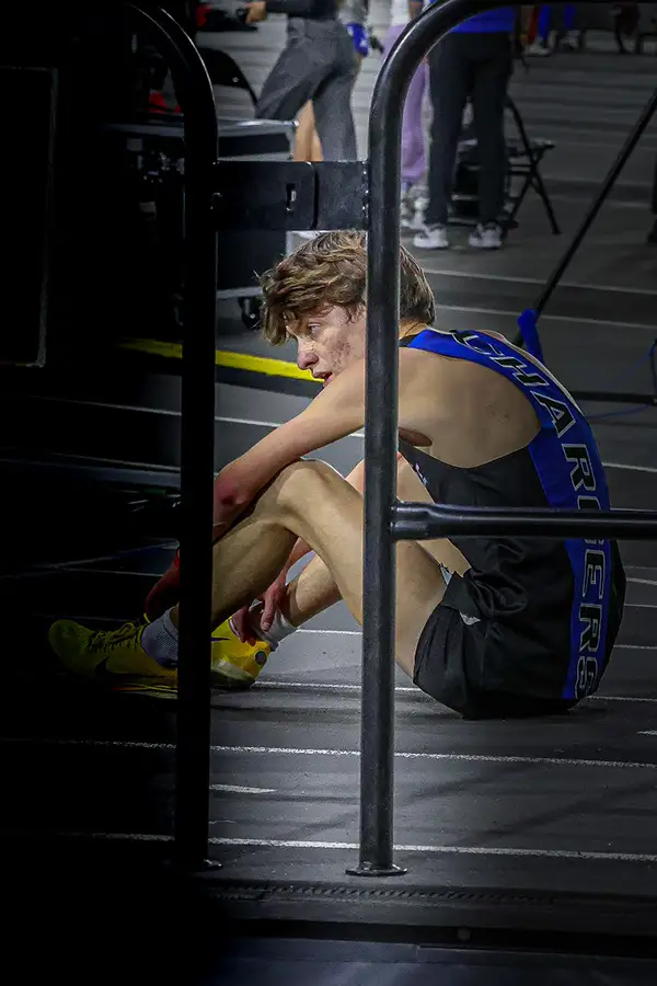 Runner sitting against a railing in the dark after an indoor race