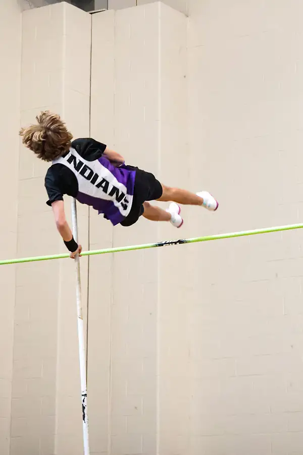 Pole vaulter in an Indians jersey arching over the bar