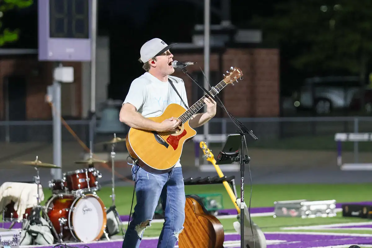 Singer with an acoustic guitar performing on an outdoor stage