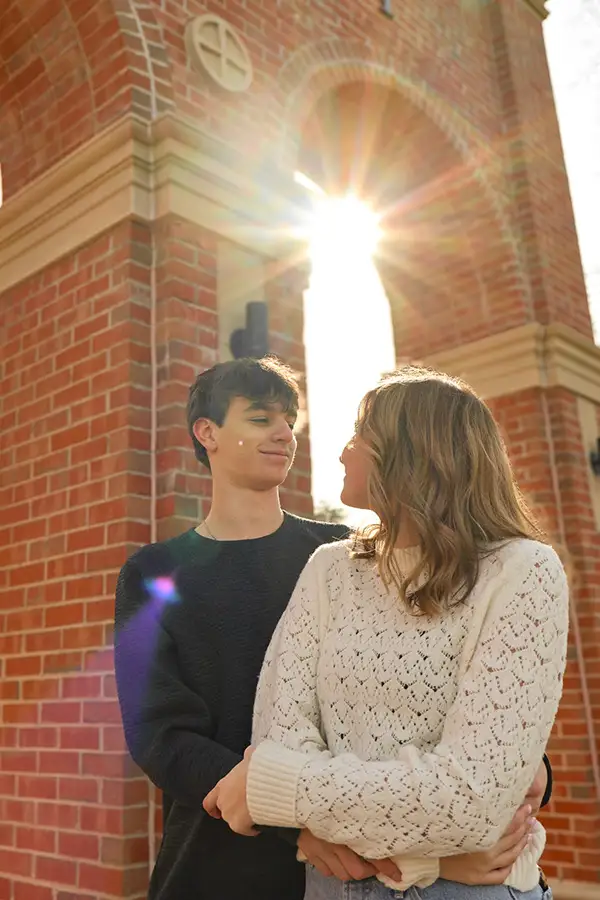 Couple facing each other by a brick arch, sun bursting through
