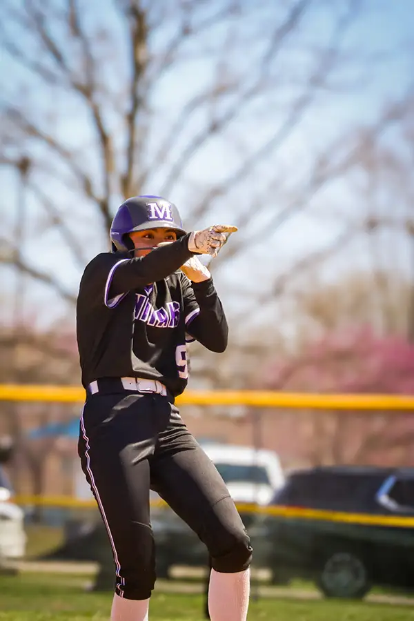 Softball player in an Indians uniform pointing from the base path