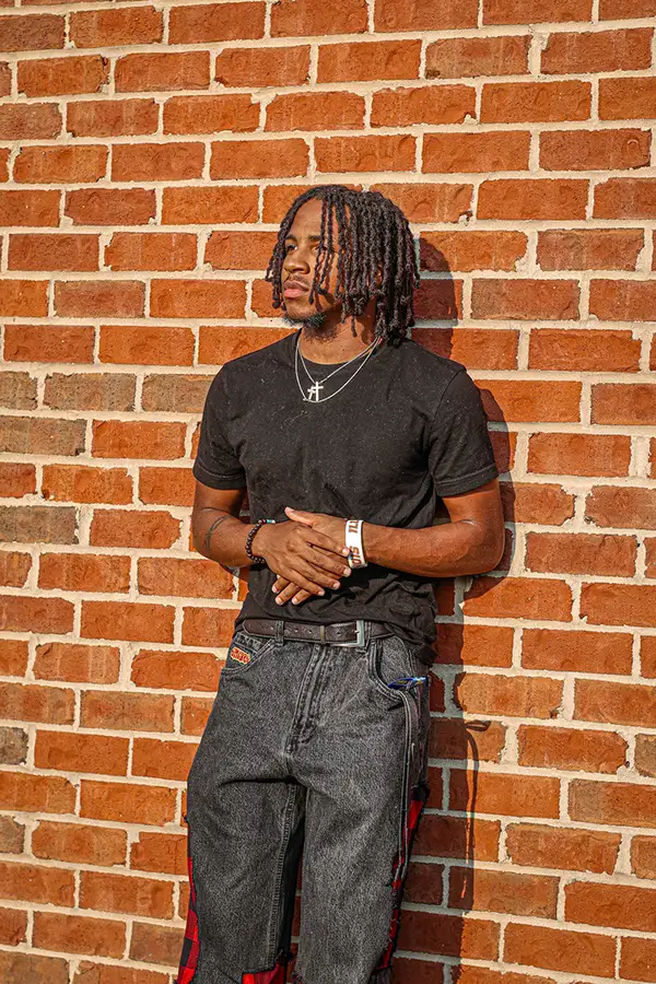 Young man in black leaning against a red brick wall