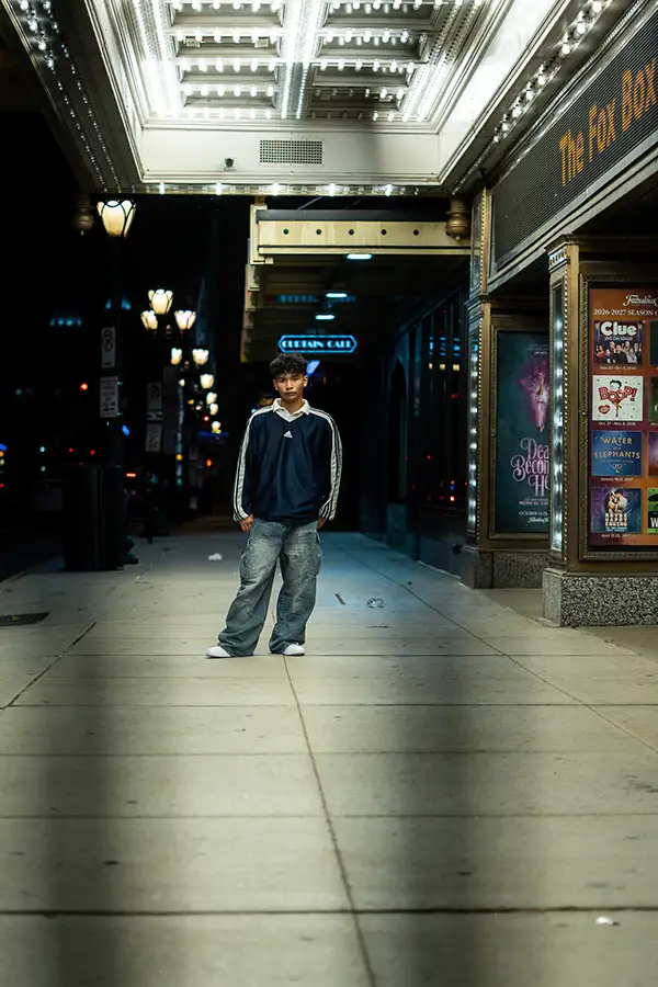 Young man standing under a lit theater marquee at night