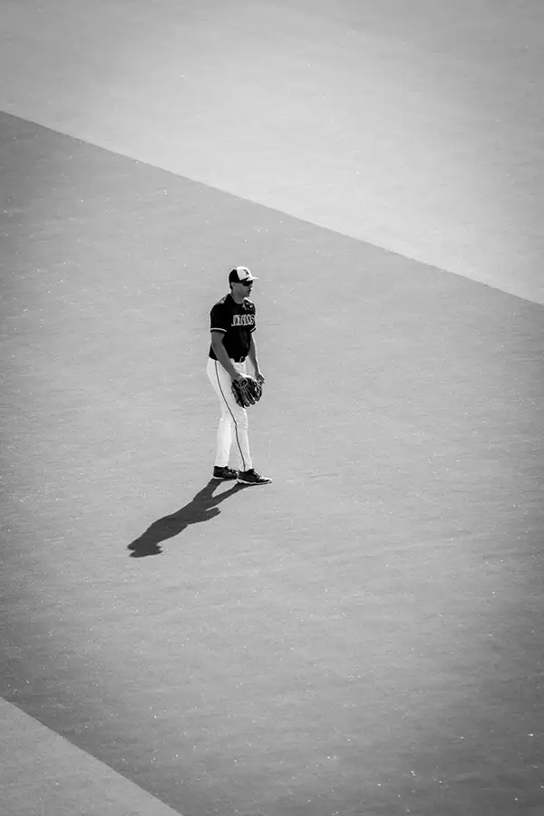 Lone baseball player on a pale field, long shadow stretching out