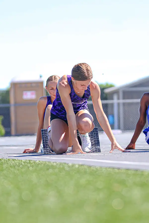 Runner in purple crouched at the start line on a grass course